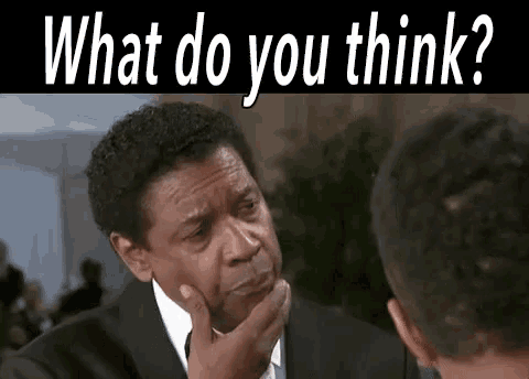 a man in a suit and tie is holding his hand to his chin and looking at another man .