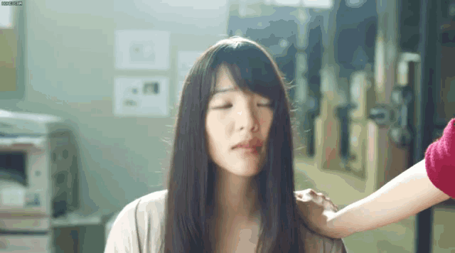 a woman with long hair is sitting down with her eyes closed and a woman is putting her hand on her shoulder .