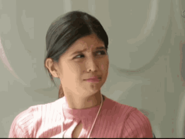 a woman in a pink sweater is making a sad face