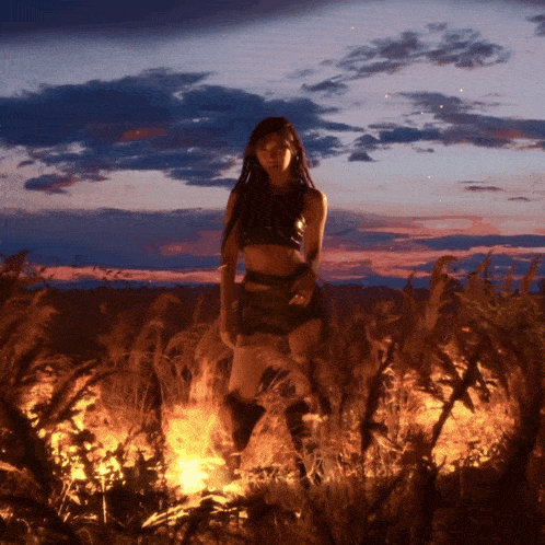 a woman in a crop top and shorts is standing in a field of burning grass