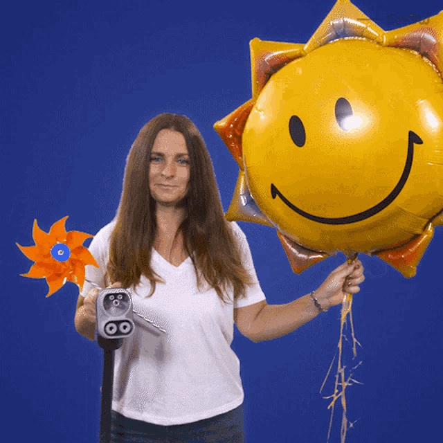 a woman is holding a windmill and a balloon with a smiley face on it