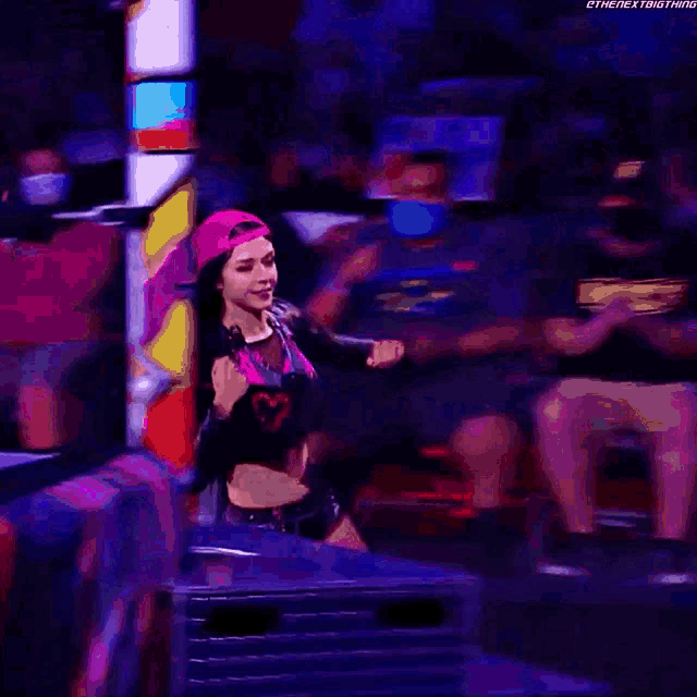 a woman in a pink hat is holding a microphone while dancing on a stage .