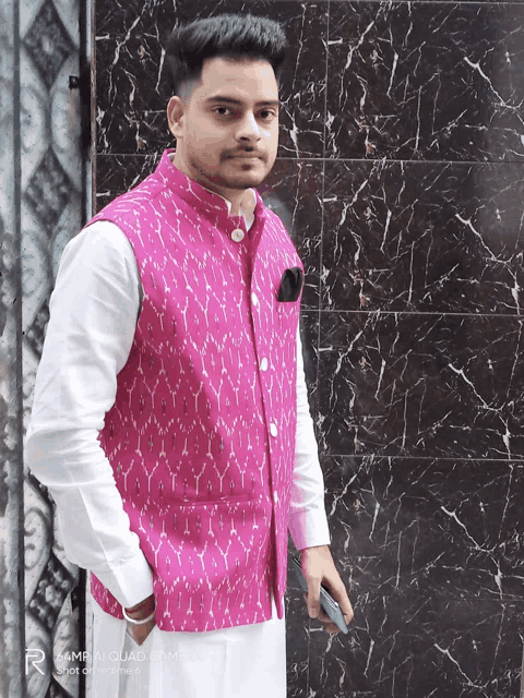 a man wearing a pink vest is standing in front of a black wall