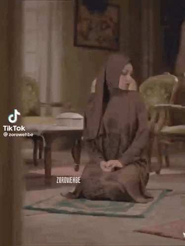a woman in a hijab is kneeling down on a prayer mat in a living room .