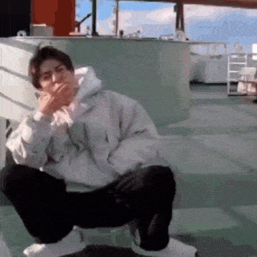 a man is sitting on the floor smoking a cigarette and covering his mouth with his hand .
