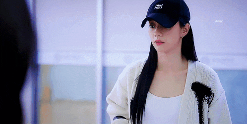 a woman wearing a black hat and a white sweater is standing in front of a mirror .