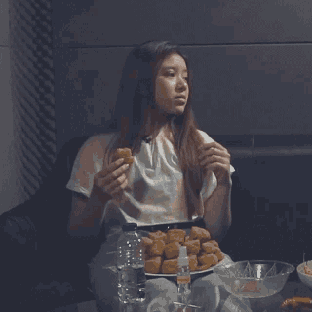 a woman is sitting at a table eating nuggets and a bottle of water