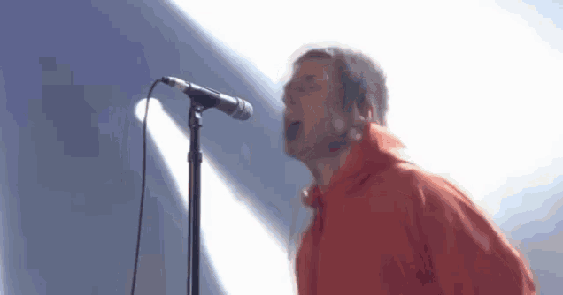 a man in an orange jacket is singing into a microphone on a stage .