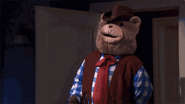 a teddy bear wearing a cowboy hat and vest is standing in a doorway