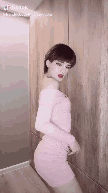 a woman in a pink dress is standing in front of a wooden wall with tiktok written on the bottom right
