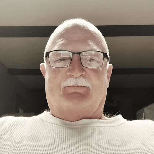 a man wearing glasses and a white sweater looks at the camera