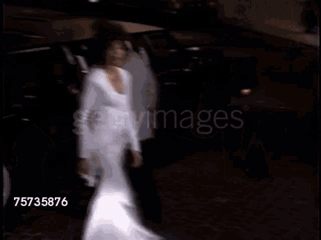 a woman in a white dress is walking towards a car
