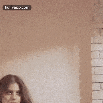 a woman is standing in front of a brick wall .