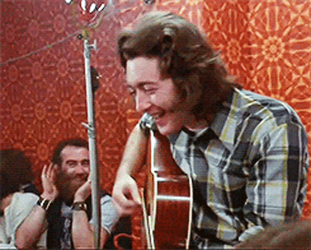 a man in a plaid shirt is playing a guitar
