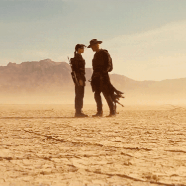 a man and a woman standing in the middle of a desert