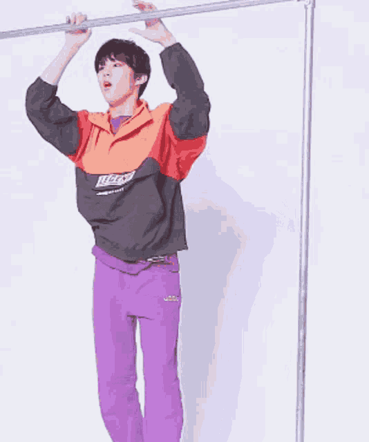 a man wearing purple pants and an orange jacket is hanging upside down on a bar