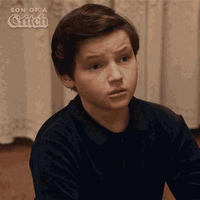a young boy is sitting in front of a curtain with the words son of a grifch behind him
