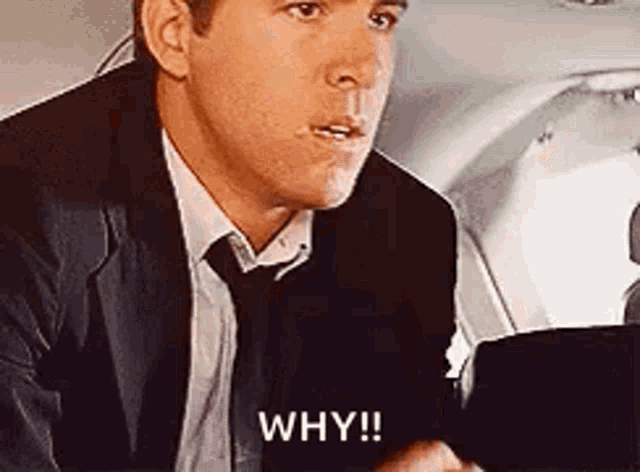 a man in a suit and tie is sitting on a plane and saying why !