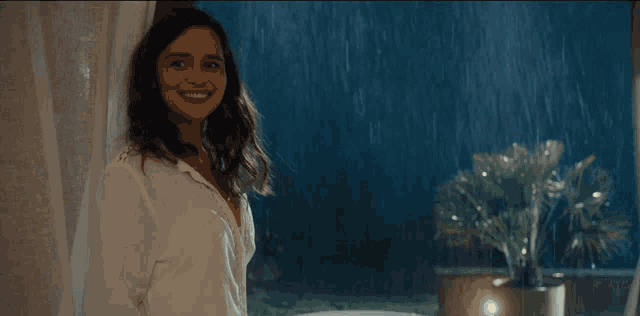 a woman in a white robe is standing in the rain looking out a window