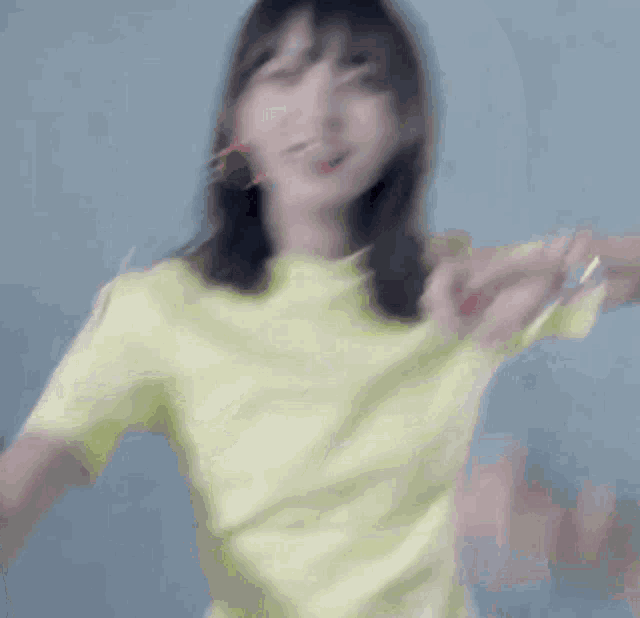 a woman in a yellow t-shirt is dancing in front of a blue background .