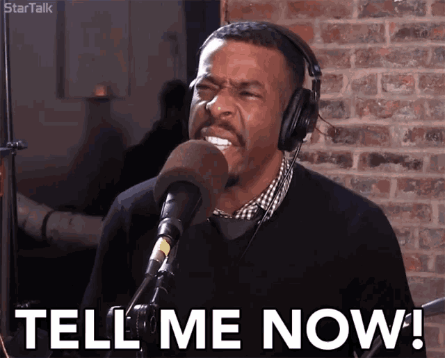 a man wearing headphones is singing into a microphone with the words tell me now behind him