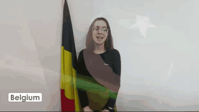 a woman stands in front of a flag with the word belgium on the bottom right