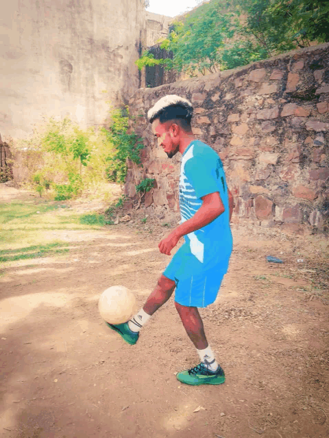 a man kicking a soccer ball wearing a blue shirt that says ' soccer ' on it