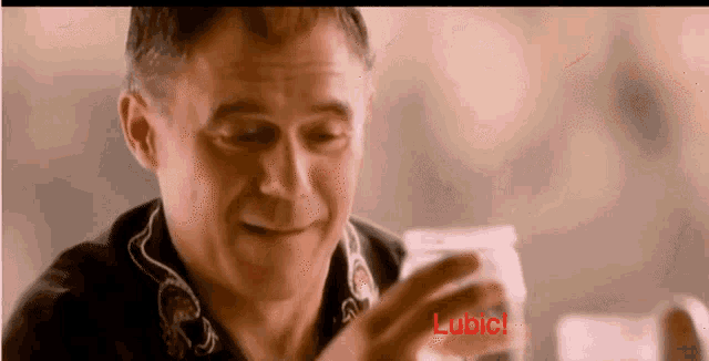 a man in a black shirt is smiling and holding a glass with the word lubic on it
