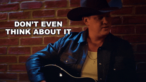 a man in a cowboy hat is singing in front of a brick wall with the words " don t even think about it "
