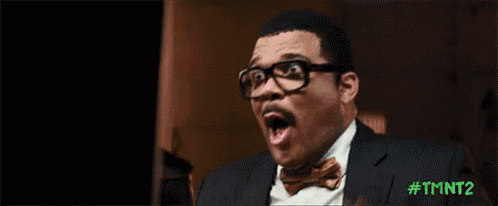 a man wearing glasses and a bow tie is sitting in front of a computer screen with his mouth open .