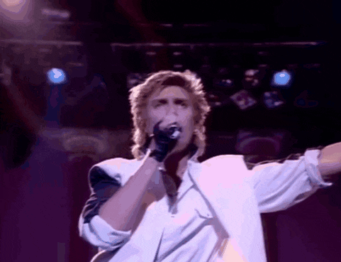 a man in a white shirt is singing into a microphone on a stage