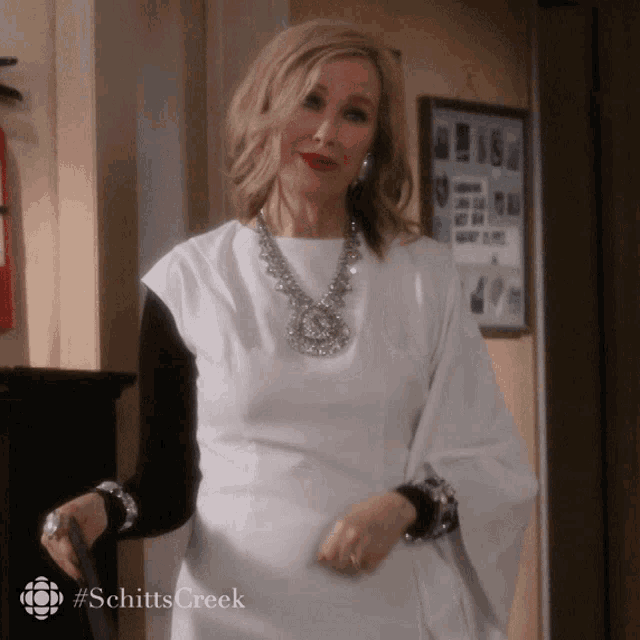 a woman is wearing a white dress and a necklace with the hashtag schittscreek on the bottom