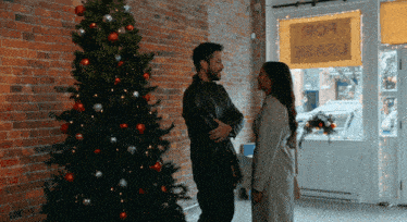 a man and woman standing in front of a christmas tree in front of a sign that says for sale