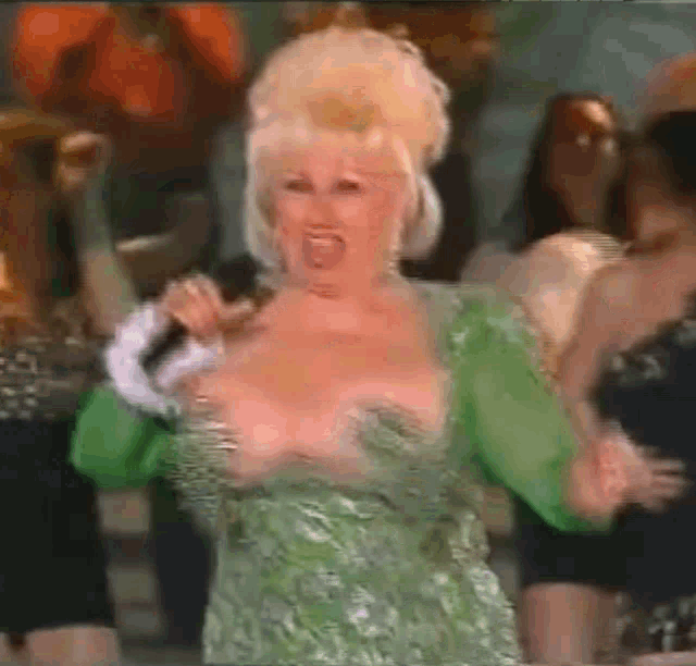 a woman in a green dress is singing into a microphone while dancing in front of a crowd .