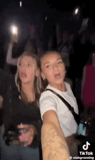 two girls are taking a selfie in a dark room while holding drinks .