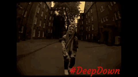 a woman with dreadlocks is dancing in front of a brick building with #deepdown written in red