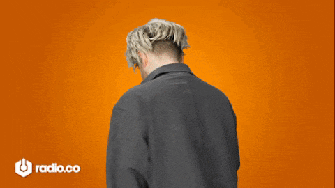 a man wearing a wig is standing in front of an orange background with radio.co written on it
