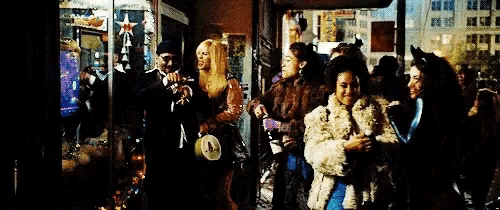 a group of people in fur coats are standing in front of a store window .