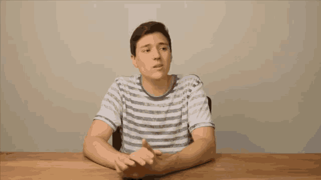 a man in a striped shirt sitting at a table with his hands folded