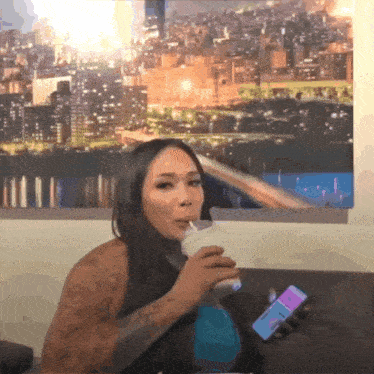 a woman drinking a milkshake while holding a phone that says ' i love you ' on it
