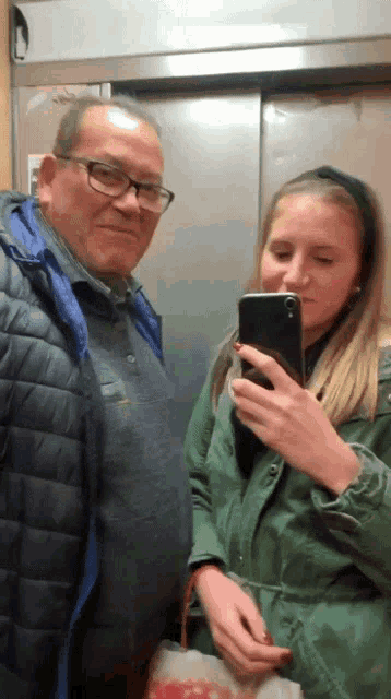 a man and a woman are in an elevator and the woman is taking a picture of herself