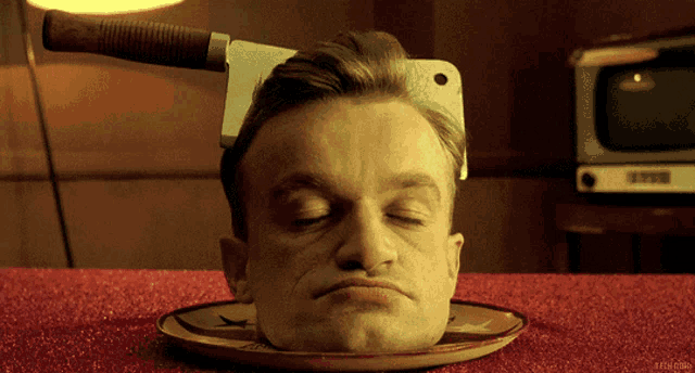 a man 's head is on a plate with a cleaver on it