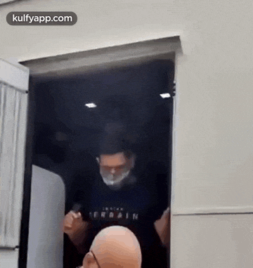 a bald man wearing a mask and glasses is standing in a doorway .
