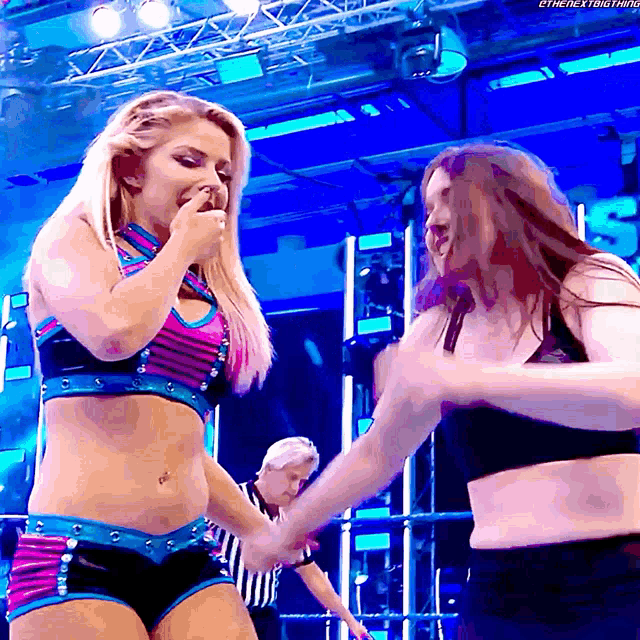 two female wrestlers are holding hands in a ring with a referee behind them and the words the next thing on the bottom right