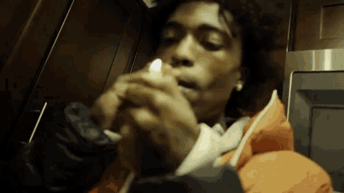 a man in an orange jacket is lighting a cigarette in front of a microwave