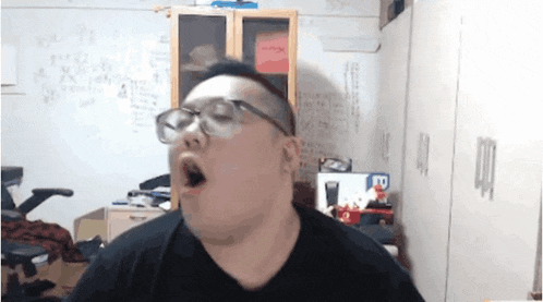 a man wearing glasses and a black shirt is yawning in a room