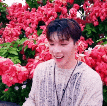 a young man is standing in front of a bush of pink flowers and smiling .