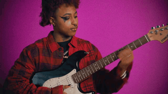 a woman in a plaid shirt is playing a squier guitar on a purple background