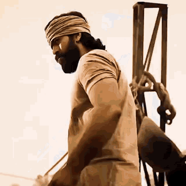 a man with a beard and a bandana on his head is standing in front of a metal structure .