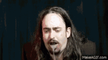a man with long hair and a beard is holding a microphone in his mouth .